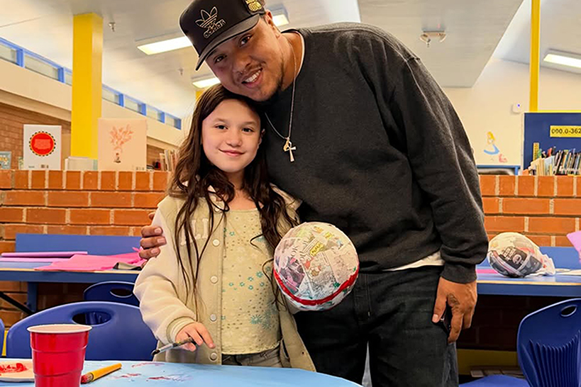 A girl smiles as she holds her papier mache ornament next to her dad