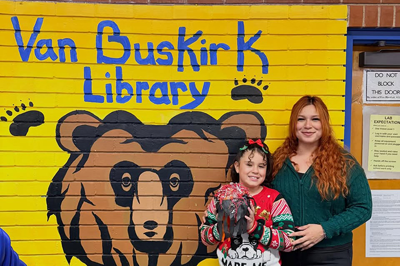 A girl and her mom stand in front of the Van Buskirk Library mural