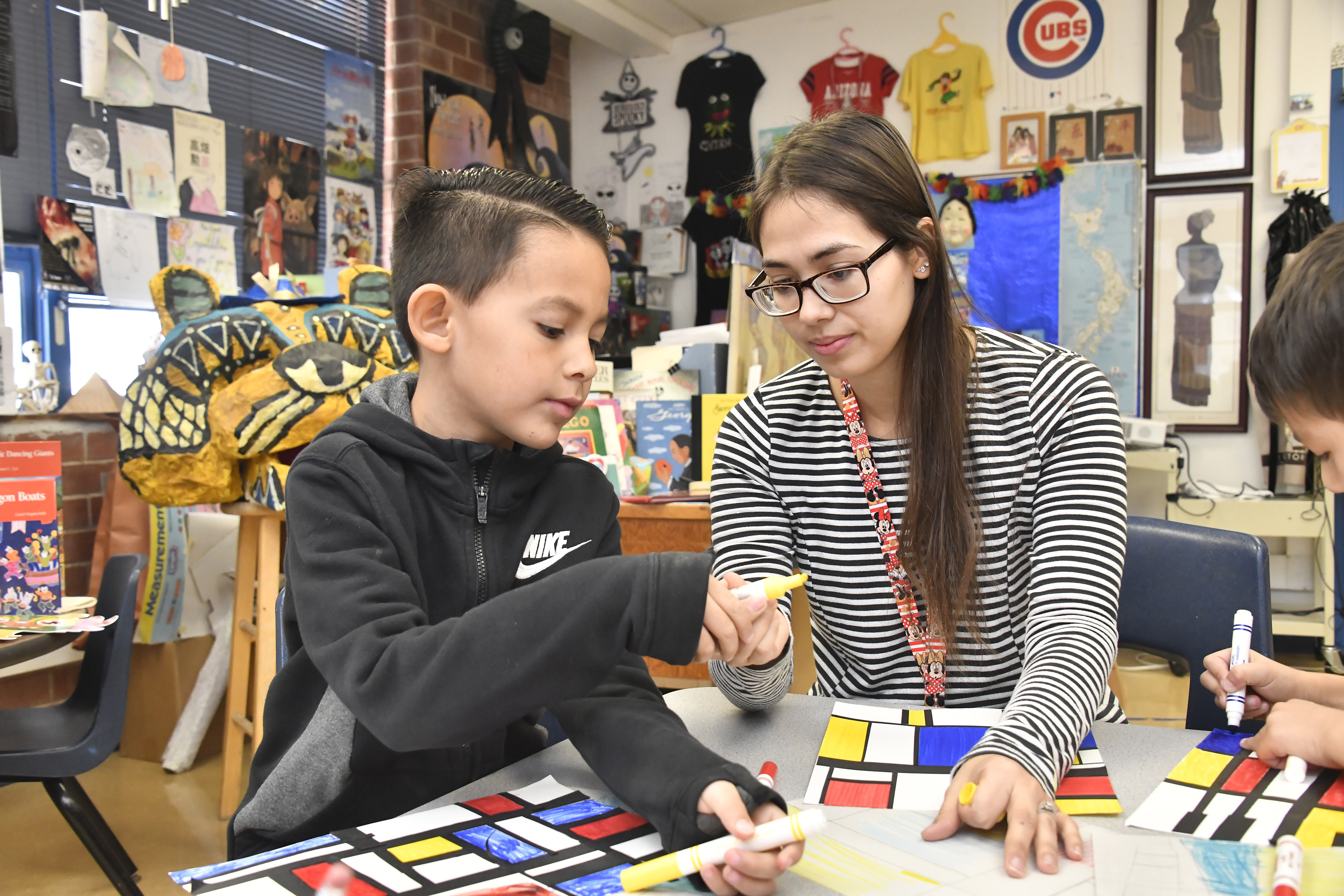 A little boy works on a project while his teacher helps him